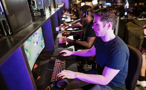 Fiatal játékos headsetet viselve versenyszerű videojátékot játszik PC-n egy e-sport arénában.