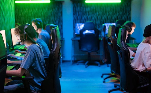 Játékosok csoportja PC-ken játszik egy modern, neonvilágítással és ergonomikus székekkel felszerelt e-sport játékteremben.