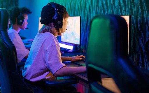 Női játékos headsetet visel, és videojátékot játszik PC-n egy neonfényes játékteremben, fókuszált, versenyszerű légkörben.